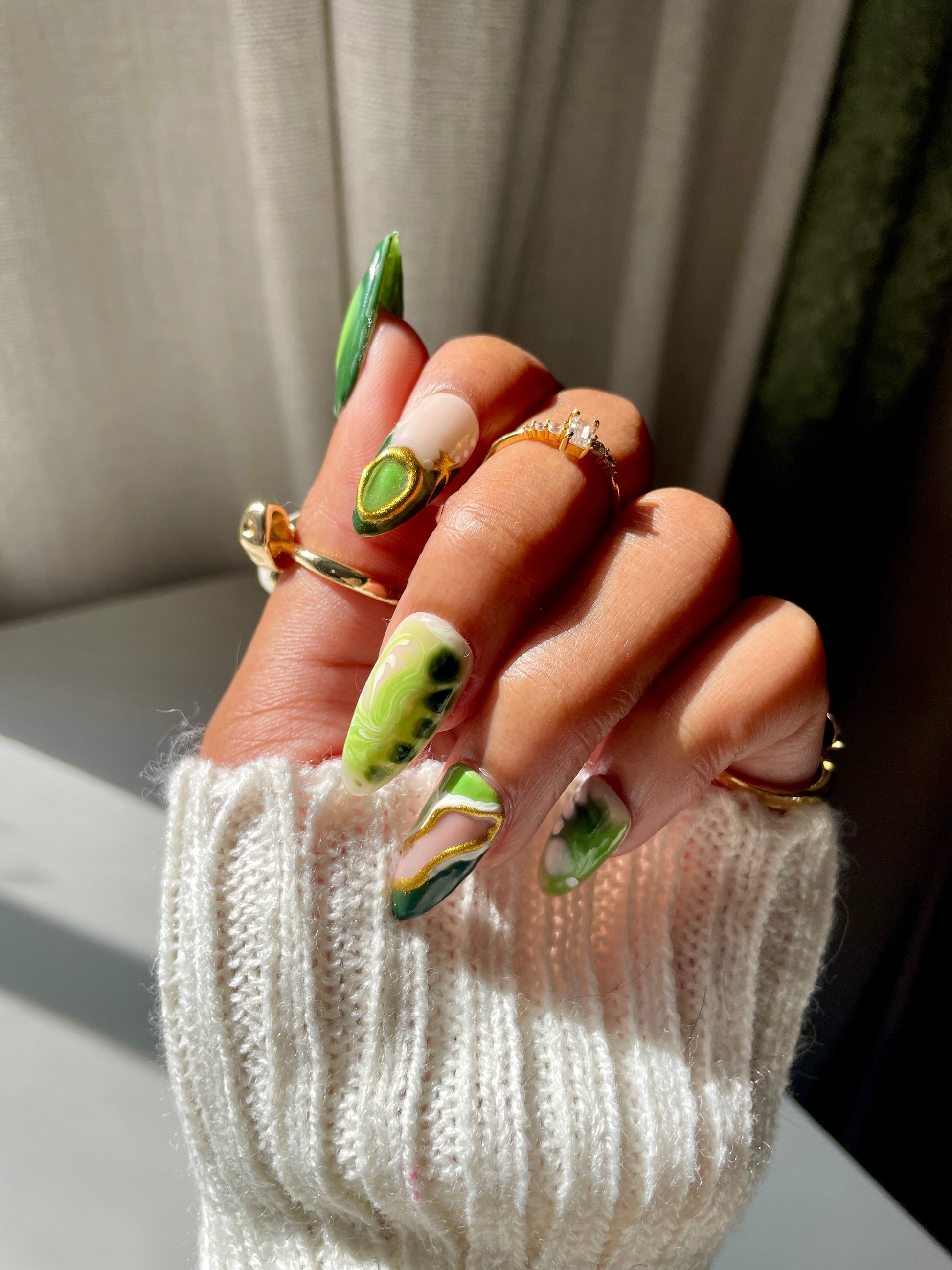 Hand with green nail polish and multiple rings on a neutral background