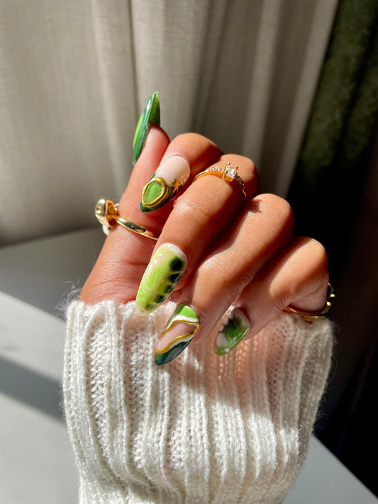 Hand with green nail polish and multiple rings on a neutral background